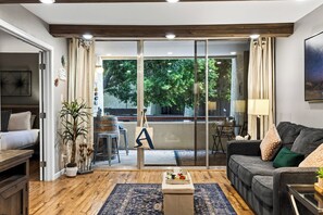 A modern living room with a sofa, coffee table, and a view through a glass door to an outdoor area with a dining table. - Resort Pool + Spa + Balcony | Fashion Square + Echo Canyon | Camelback Cabana (Scottsdale)