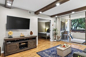 A living room with a flat-screen TV, wooden entertainment unit, and a coffee table with a tray of fruit. - Resort Pool + Spa + Balcony | Fashion Square + Echo Canyon | Camelback Cabana (Scottsdale)