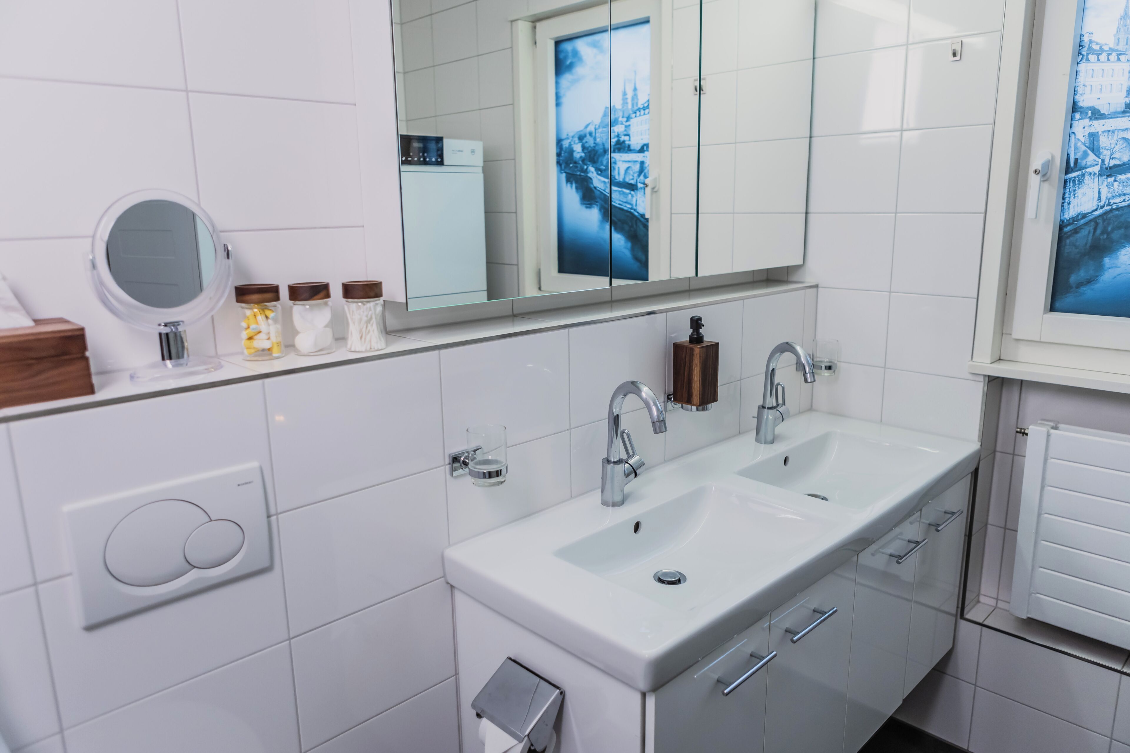 A modern bathroom with a double sink, a mirror, and a toilet paper holder.