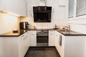 A compact kitchen with white cabinets, a black range hood, a built-in oven, and a stainless steel sink. - Stylish penthouse in the old town with generous rooftop terrace facing city hall (Basel)