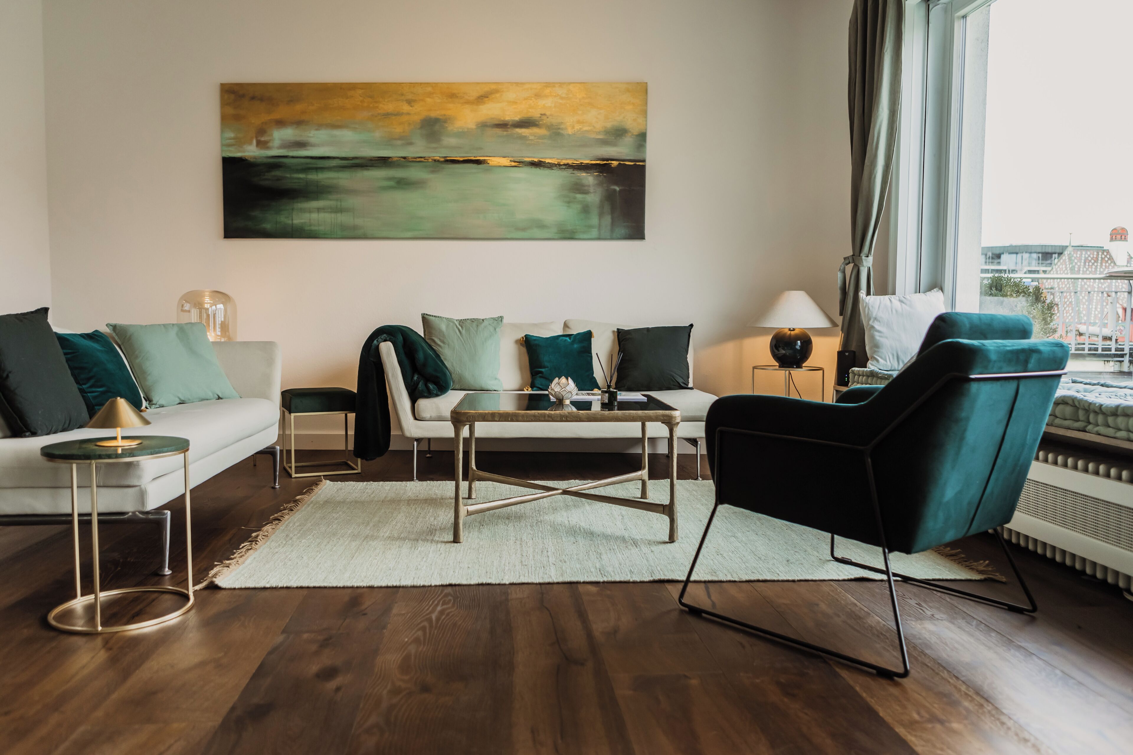 A modern living room with a sofa, armchair, coffee table, and a painting on the wall.