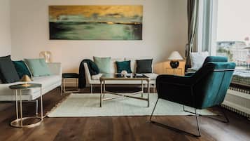 A modern living room with a sofa, armchair, coffee table, and a painting on the wall.