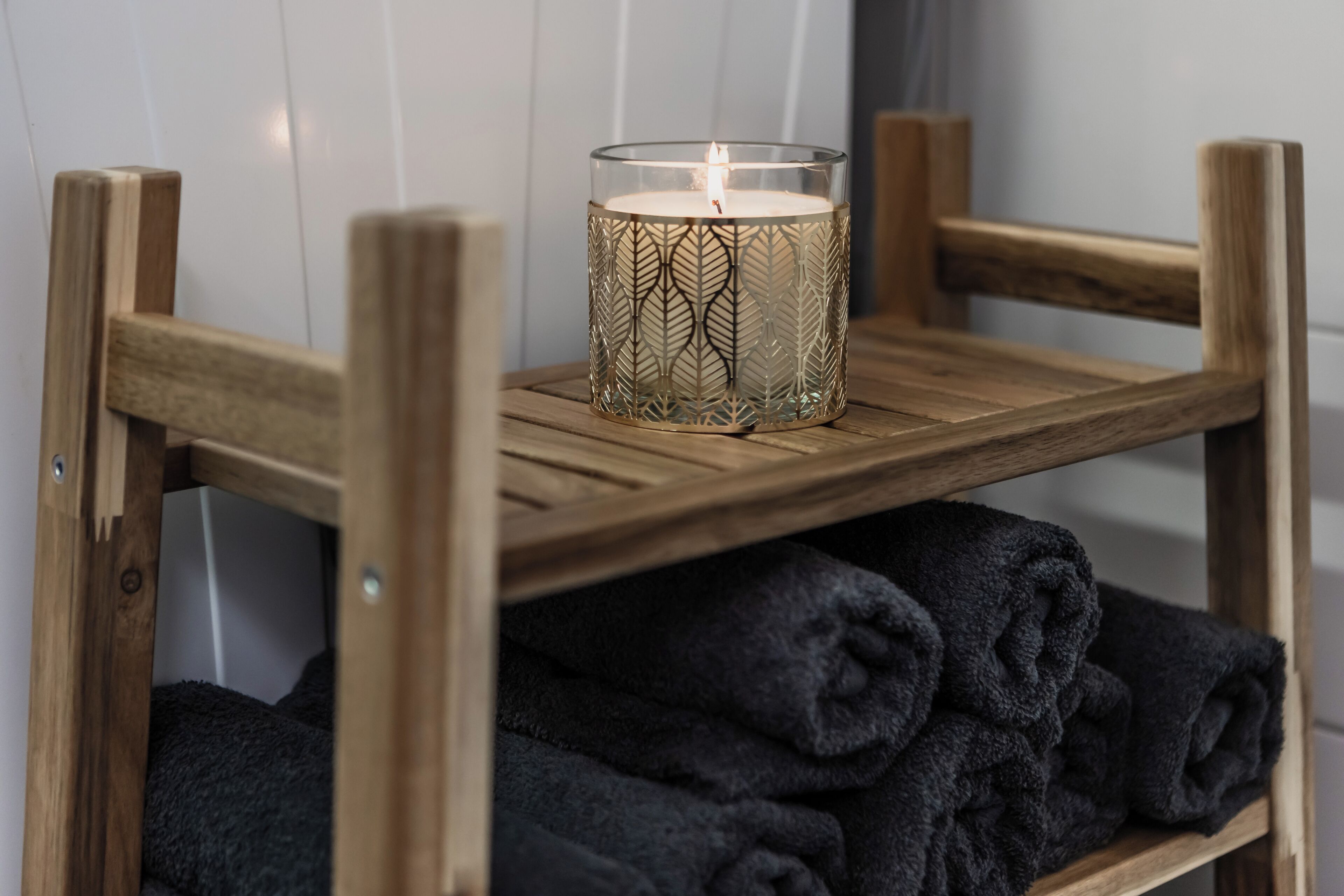 Ein Holzsessel mit Ablage für zusammengerollte Handtücher und einem Kerzenhalter mit brennender Kerze.