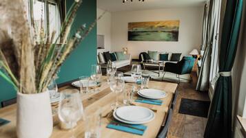 A dining area with a wooden table set for a meal, a sofa in the background, and a painting on the wall.
