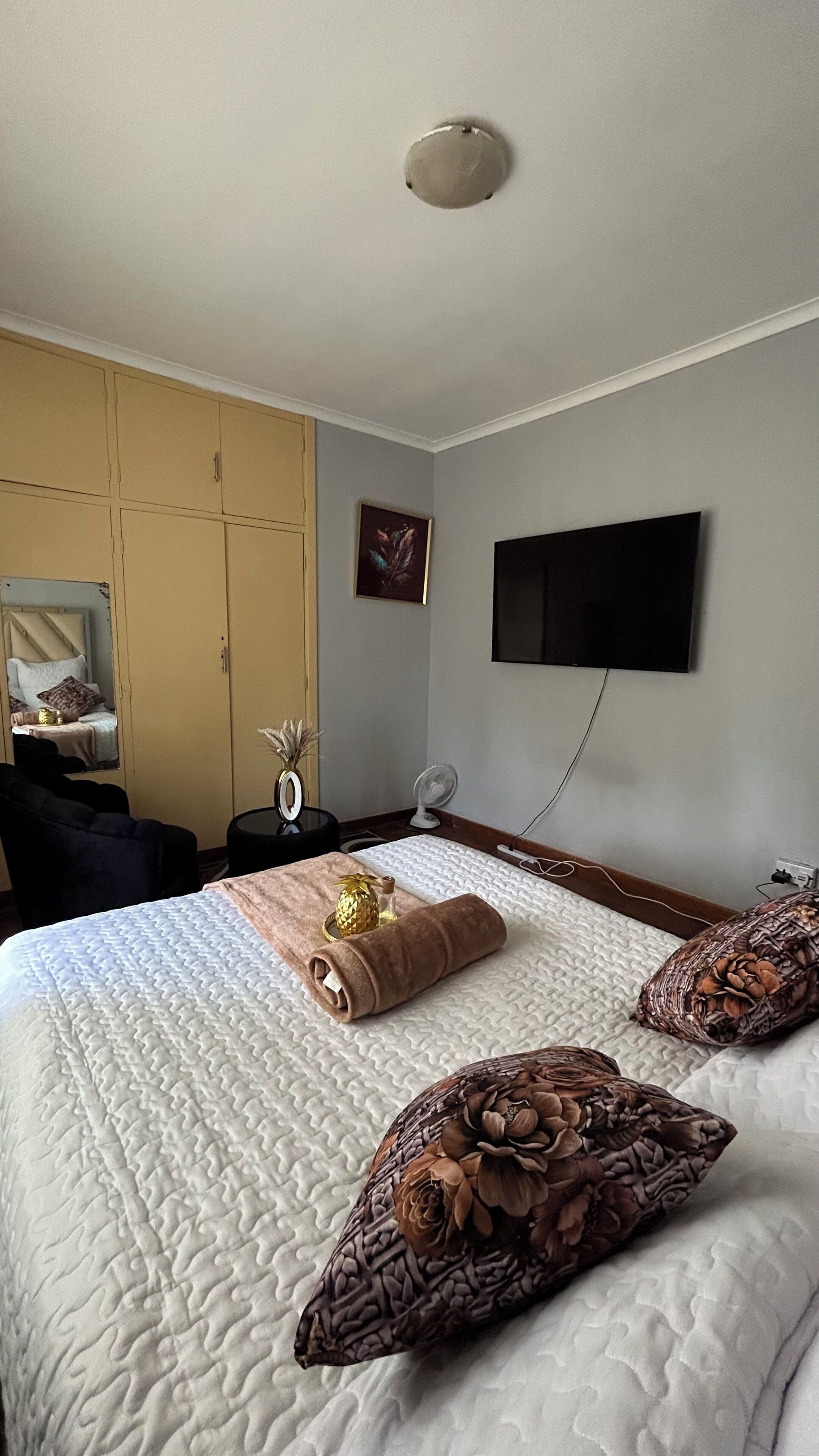 Una habitación de hotel con una cama, un televisor de pantalla plana montado en la pared, una mesita de noche con lámpara y un armario.
