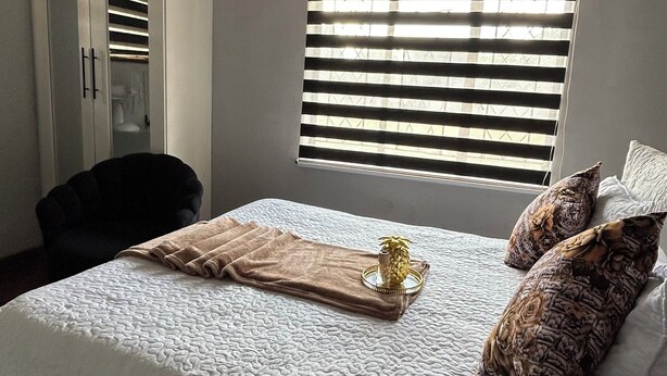 Un dormitorio con cama, armario, ventana con persianas y una silla.