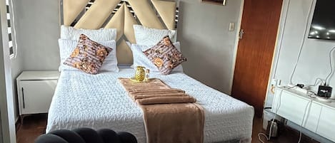 Una habitación de hotel con cama, mesita de noche, televisor y una silla.