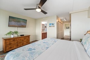 Une chambre à coucher avec un lit, une commode, un ventilateur de plafond et un tableau accroché au mur.