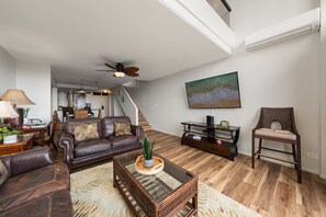 Un salon spacieux avec un canapé en cuir, une table basse en verre et un tableau représentant une scène de plage.