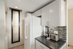 A kitchen with white cabinets, a black countertop, a built-in toaster, and a refrigerator. - Charming 2BD w Ocean Views Near Beach - KV F401 (Lahaina)