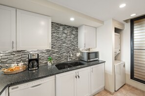 A modern kitchen with white cabinets, a black countertop, a coffee maker, a microwave, and a sink. - Charming 2BD w Ocean Views Near Beach - KV F401 (Lahaina)
