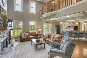 A spacious living area with a high ceiling, a fireplace, a dining area with a kitchen, and a balcony with a wooden railing. - Day Trip to Nashville! Large Home on 5 Acres (Springfield)