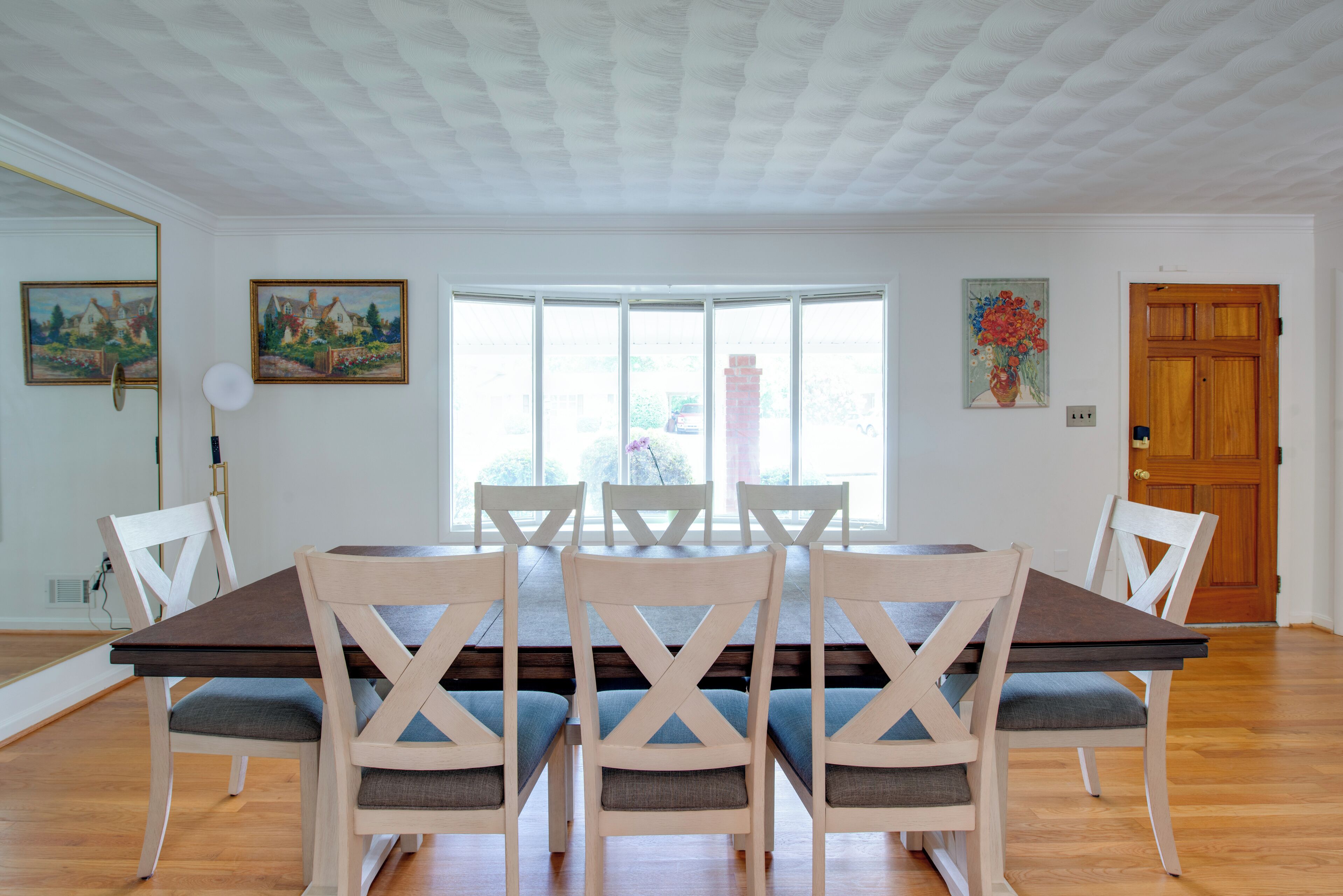 A dining room with a large table, six chairs, and a wooden door.