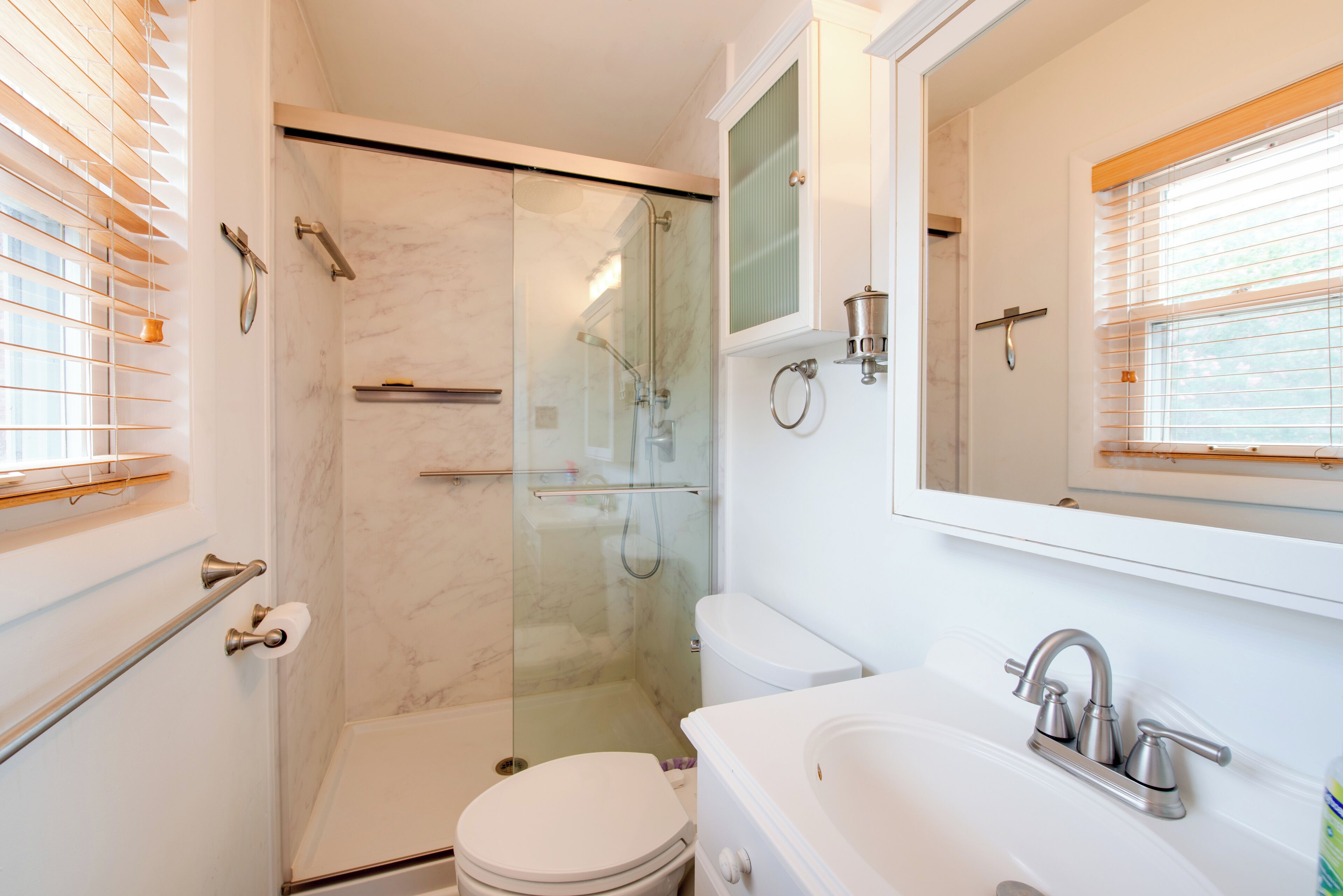 A bathroom with a glass-enclosed shower, a toilet, a sink with a faucet, and a mirror above the sink.