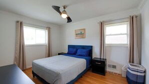 Une chambre à coucher avec un lit, une table de chevet, un ventilateur de plafond et une fenêtre avec des rideaux.