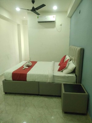 A bedroom with a bed, a bedside table, a ceiling fan, and an air conditioning unit. - Sakas Manor Guest Rooms (Hyderabad)