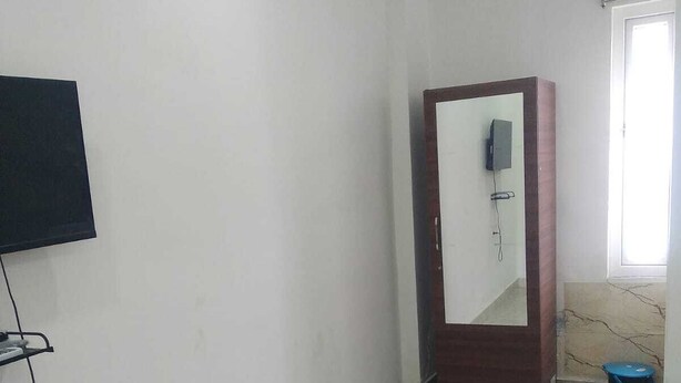 A room with a tiled floor, a wooden door, a television mounted on the wall, and a window with a view. - Sakas Manor Guest Rooms (Hyderabad)