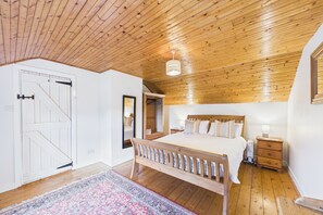 A bedroom with a wooden ceiling, a bed with a wooden headboard, a bedside table, a nightstand, and a mirror on the wall.