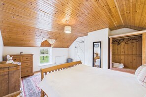 Ein Schlafzimmer mit Holzboden, einem Bett, einem Schminktisch, einem Heizkörper und einem Kleiderschrank mit Kleiderbügeln.