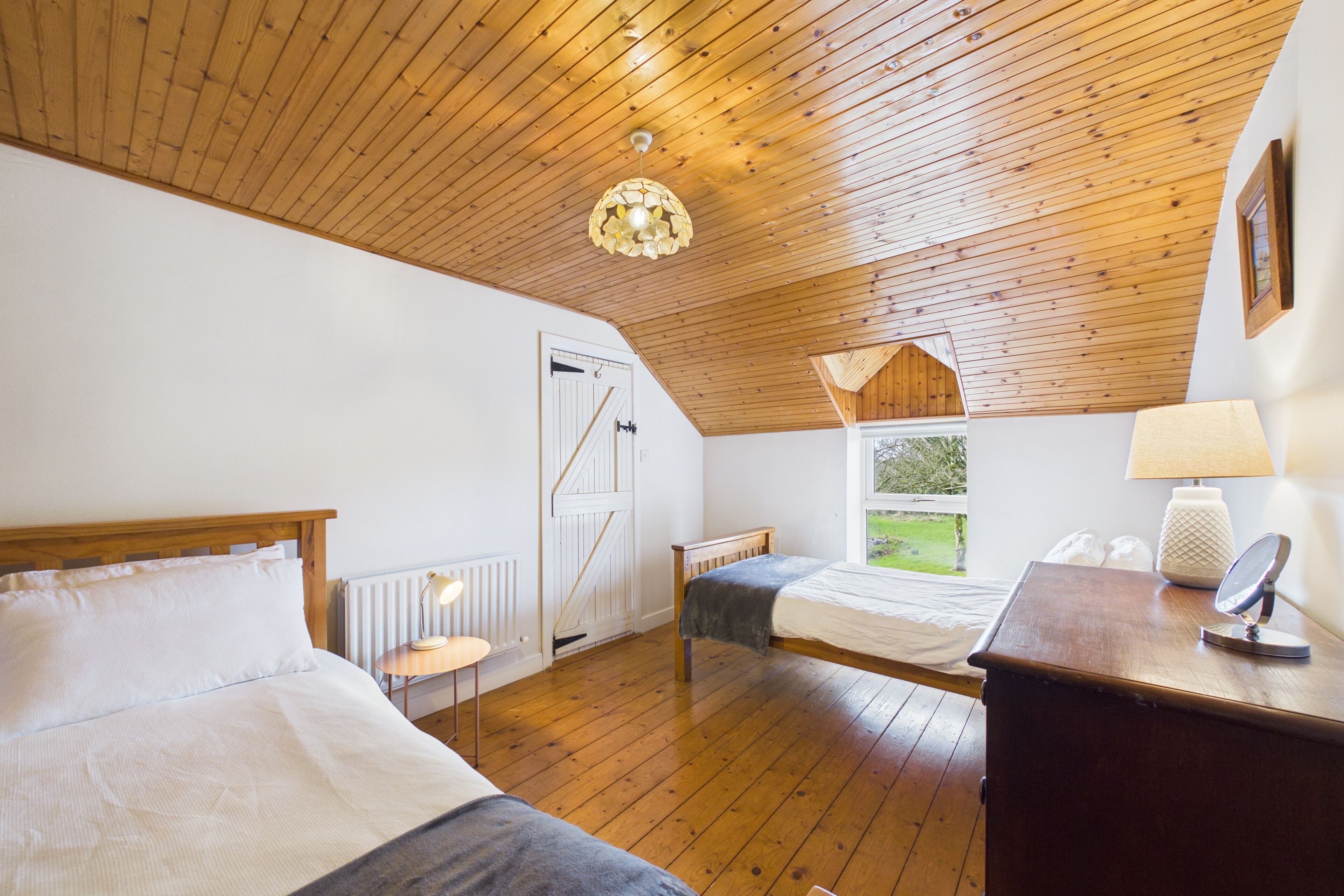 Une chambre avec deux lits, un plafond en bois, une fenêtre donnant sur un beau paysage et une table de chevet avec une lampe.