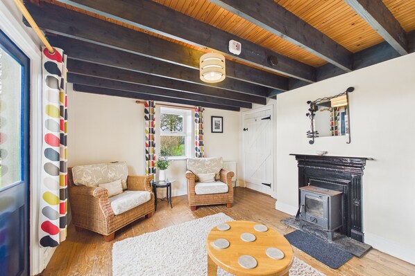 A cozy living room with wicker furniture, a fireplace, and a view through a window.
