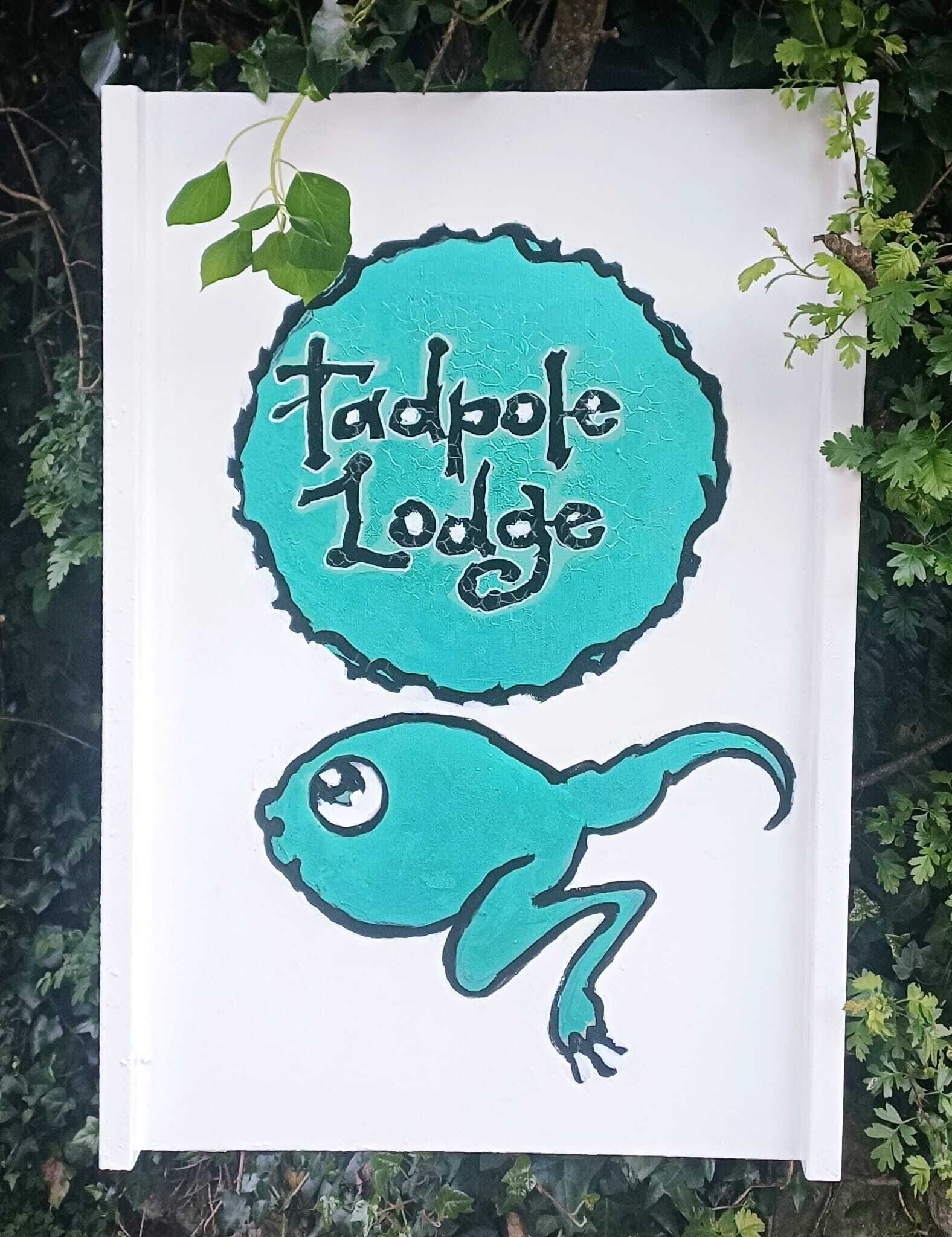 Een bord met de tekst 'Tadpole Lodge' en een gestileerde kikkerillustratie.