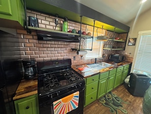 A kitchen with a brick backsplash, green cabinets, a stove, and a coffee maker. - The Green Room, Music-Themed Tiny Home Near Lake Travis (Austin)