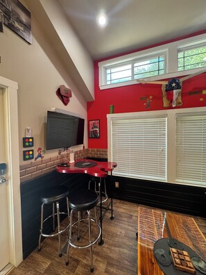 A kitchen with a red accent wall, a black countertop, and a bar area with stools. - The Green Room, Music-Themed Tiny Home Near Lake Travis (Austin)