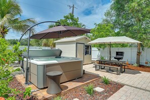 Un jacuzzi con toldo, una parrilla y una mesa de picnic en un patio trasero.