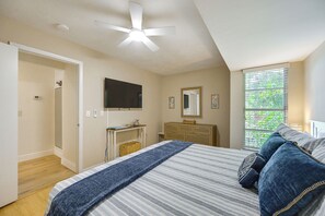 Ein Schlafzimmer mit einem Bett, Deckenventilator, einem Schminktisch, einem Fernseher und einem Fenster mit Blick auf Grünflächen.