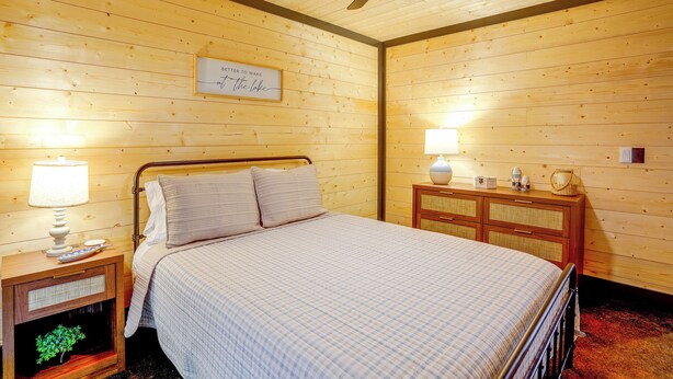A bedroom with a bed, bedside lamps, a ceiling fan, a wooden dresser, and a framed sign on the wall. - Walk to the Water! Kentucky Lake Cabin (Murray)