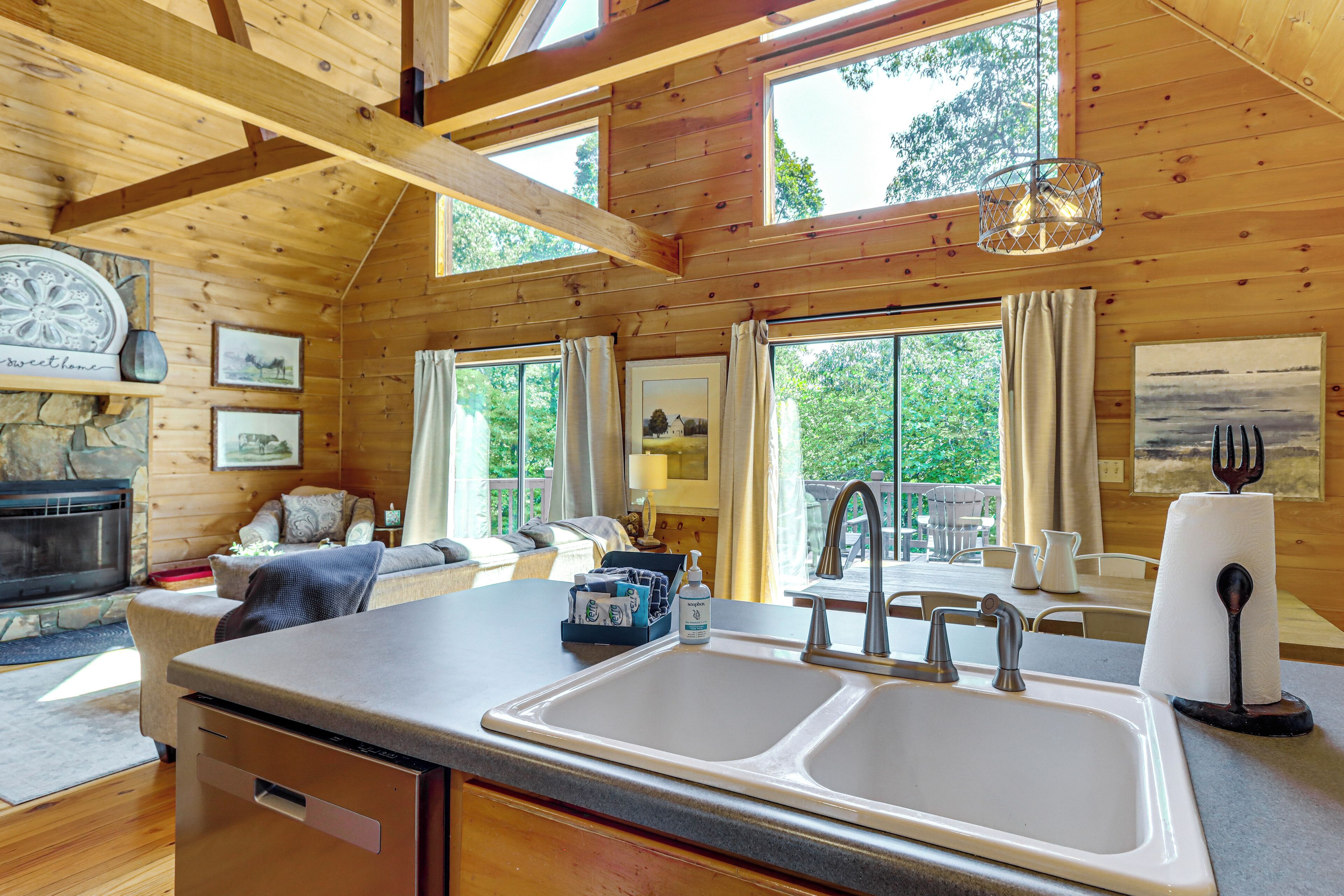 Interior de uma cabana de madeira com cozinha, incluindo uma pia dupla, área de jantar com mesa e cadeiras, e um espaço de estar aconchegante com lareira.