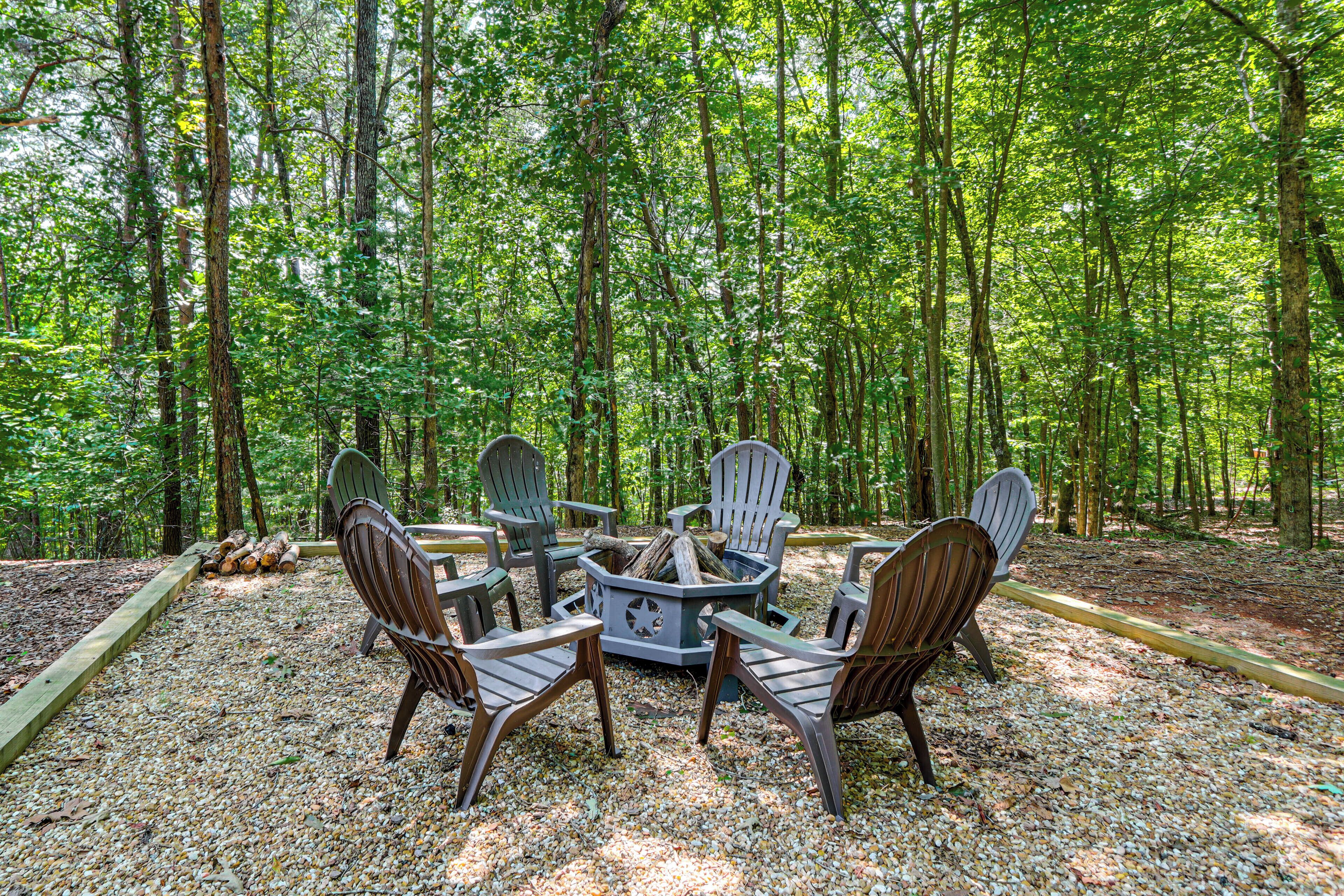 A circular arrangement of Adirondack chairs around a central fire pit in a forested area.