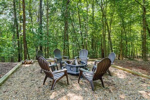 A circular arrangement of Adirondack chairs around a central fire pit in a forested area. - Ellijay Cabin | Hot Tub, Mtn Views & Game Room (Ellijay)
