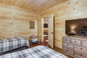 Ein Zimmer in einer Holzhütte mit zwei Betten, einem Schminktisch und einem Fernseher.