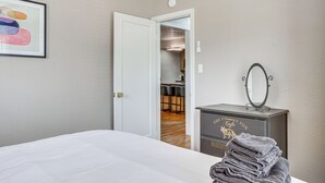 Ein Hotelzimmer mit einem aufgeräumten Bett, einem Schminktisch mit Spiegel und einem gerahmten Bild an der Wand.