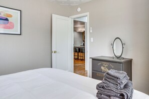 A hotel room with a neatly made bed, a dresser with a mirror, and a framed picture on the wall.
