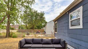Ein Garten mit einer dunkelgrauen Outdoor-Sofa und einem quadratischen Tisch mit Feuerstelle.