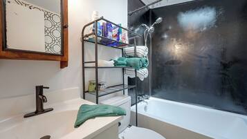 A bathroom with a white sink, a toilet, a bathtub, and a shower with a glass door. There is a towel rack with folded towels and a shelf with toiletries.