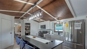 A modern kitchen with a central island, stainless steel appliances, and a hanging light fixture. - Hot Tub + Dock! Lakefront Angler's Oasis in Irons (Irons)
