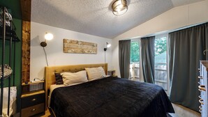 A bedroom with a bed, two bedside lamps, a wooden headboard, a wall-mounted artwork, and a window with curtains. - Hot Tub + Dock! Lakefront Angler's Oasis in Irons (Irons)