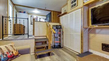 A compact living space with a kitchenette, a television mounted on the wall, and a staircase leading to an upper level.
