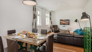 Ein Essbereich mit einem Glastisch, Stühlen, Frühstücksangebot und einer Couch im Hintergrund.