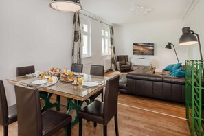 A dining area with a glass table, chairs, breakfast items, and a sofa in the background. - Villa Hohe Buchen, Apartment 02 with a garden, just 150 m from the beach - Beautiful (Heringsdorf)