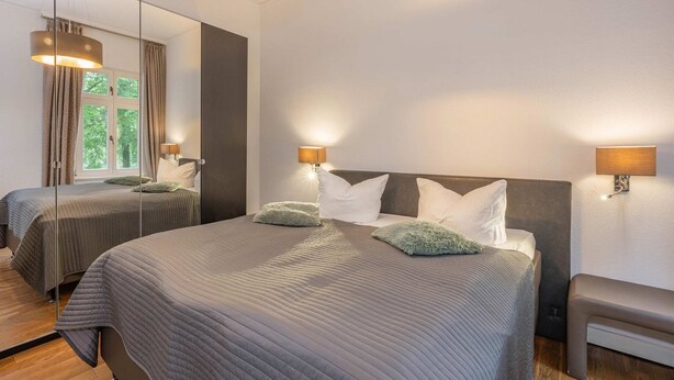 Quarto de hotel com duas camas, um espelho grande e luminárias fixadas na parede.