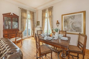 Ein Esszimmer mit Holztisch, gedeckt für vier Personen, umgeben von gepolsterten Stühlen. Ein großes gerahmtes Kunstwerk hängt an der Wand, und im Hintergrund ist eine Vitrine mit Glastüren zu sehen.