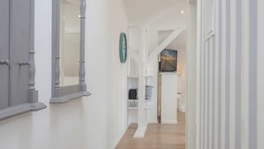 Um corredor com piso de madeira, paredes brancas e um relógio na parede.