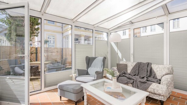 A conservatory with a sofa, armchair, ottoman, and a table with a vase. - Villa Westfalia, Apartment 04, just 150 m from the beach, with a terrace - Cozy vacation rental in (Heringsdorf)