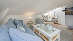 Quarto estilo loft moderno com teto inclinado, um sofá, uma cadeira, uma mesinha e um aparador.