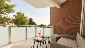 Ein Balkon mit Korbmöbeln, einem Glastisch und einem Getränk.